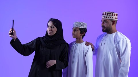 قضاء اوقات ممتعه مع العائلة , توثيق اللحظات السعيدة مع الأبناء, استخدام جهاز تقني حديث ومتطور, تصوير لامرأة عربية خليجية امارتية محجبة ترتدي عباءة سوداء مع عائلتها وتقوم بالتقاط صورة سيلفي عبر الجوال