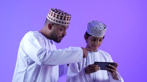 مشاهدة الافلام والقصص الالكترونية عبر جهاز الجوال ، مفهوم الالفة والانسجام والمودة بين افراد الاسرة، تصوير لعائلة عربية خليجية عمانية مبتسمة وسعيدة، استخدام الاجهزة والتقنيات الحديثة المتطورة, قضاء وقت ممتع مع العائلة