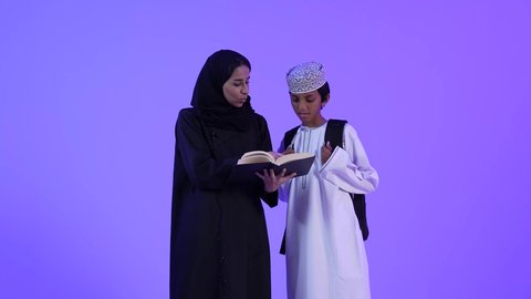 التعلم في المدارس المتطورة في سلطنة عمان، مفهوم الاجتهاد والمثابرة للوصول الى المراتب العليا، الاستعداد لبدء عام دراسي جديد، تصوير لأم عربية خليجية عمانية محجبة ترتدي عباءة سوداء تقوم بمساعدة ابنها بالتجهز للذهاب الى المدرسة