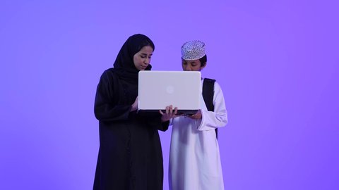 متابعة حصص الاونلاين عبر جهاز الحاسوب المحمول، أخبار جديده على مواقع التواصل الاجتماعي، تصوير لولد عربي خليجي عماني بجانب والدته يقوم بالتعلم عن بعد بإيماءات الضحك و السعادة، تشجيع الأبناء والاعتناء بهم