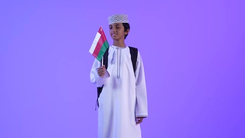 National flags and banners of Arab countries, national holidays and occasions, pride and honor in Omani symbols and flag, back to school, a picture of an Arab Gulf Omani student wearing a dishdasha and a kuma carrying a school backpack and holding the flag of the Sultanate of Oman in his hand