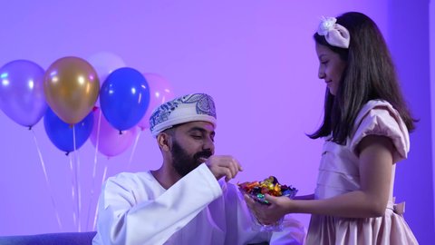 توزيع الحلويات الشعبية في الأعياد، تصوير لعائلة عربية خليجية عمانية تحتفل بالعيد المبارك، مفهوم الكرم وتقديم الضيافة العربية ، ارتداء الأزياء العمانية التقليدية،جو البهجة والفرح والزينة، طقوس الاحتفالات والمناسبات السعيدة في سلطنة عمان