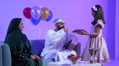 جو البهجة والفرح والزينة، توزيع الحلويات الشعبية في الأعياد، طقوس الاحتفالات والمناسبات السعيدة في سلطنة عمان، تصوير لعائلة عربية خليجية عمانية تحتفل بالعيد المبارك، ارتداء الأزياء العمانية التقليدية، مفهوم الكرم وتقديم الضيافة العربية