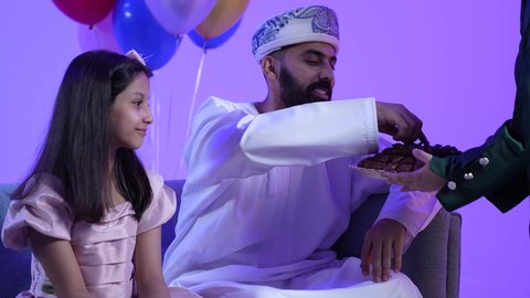توزيع الحلويات الشعبية في الأعياد، جو البهجة والفرح والزينة، طقوس الاحتفالات والمناسبات السعيدة في سلطنة عمان، تصوير لعائلة عربية خليجية عمانية تحتفل بالعيد المبارك، ارتداء الأزياء العمانية التقليدية، مفهوم الكرم وتقديم الضيافة العربية