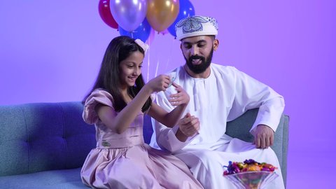 تقديم العيديات للاطفال فى العيد ، المعايدات والتهنئات وطقوس المناسبات الاسلامية في سلطنة عمان، ارتداء الأزياء العمانية التقليدية، تصوير لعائلة عربية خليجية عمانية تحتفل بالعيد المبارك، جو البهجة والفرح والزينة