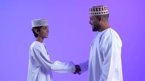 Having a good time, a picture of an Omani Gulf Arab man shaking hands with his son, gestures of joy and happiness, family visits and gatherings, happy Islamic holidays and occasions