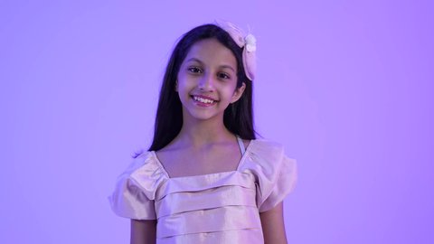 مفهوم النعومة واللطافة، الاهتمام بالمظهر الخارجي للأطفال، تصوير مقرب لطفلة عربية خليجية عمانية مبتسمة ترتدي الزي الكاجوال تنظر إلى الكاميرا بإيماءات البراءة والطفولة، بنت سعودية تقف باستقامة وثقة بالنفس