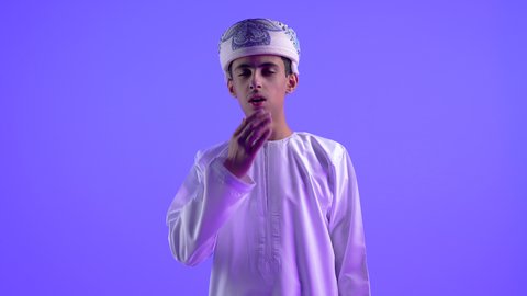 الإرهاق والتعب والحاجة للراحة، العطاس والكحه وأعراض الرشح، ضرورة أخذ العلاج المناسب، الإصابة بالزكام والانفلونزا، بورتريه لولد عربي خليجي عماني يرتدي الدشداشة والكمه العمانية يضع يده على فمه لمنع انتشار العدوى، خلفية زرقاء .