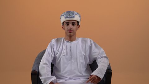 تحديد موقع معين، تصوير مقرب لولد مراهق عربي خليجي عماني يرتدي الدشداشة والعمامة يشير بأصبع السبابة الى هدف محدد، مفهوم النقر والضغط والتفاعل مع العناصر الهولوجرامية، خلفية بيج