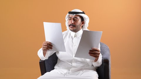 تدوين الملاحظات على الورق، تصوير لرجل عربي خليجي قطري يرتدي الزي التقليدي والشماغ ويحمل بيده قلم ومجموعة من الاوراق، التخطيط للعمل، توقيع عقد عمل، تدوين نتائج الاجتماع، اعداد تقارير ومهام العمل، دراسة جدوى الاعمال