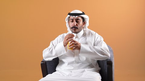 التلذذ بكوب من الشاي الساخن، محاولة الحصول على القليل من الراحة، الاسترخاء وتناول مشروبات دافئة، تصوير لشاب عربي خليجي قطري يرتدي الثوب التقليدي والشماغ يجلس على كرسي ويمسك بيده فنجان من مشروبه المفضل