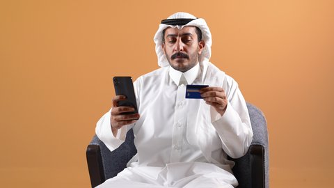 التسوق عبر الانترنت ، اجراء مكالمه هاتفيه ، دمج التقنية بالأعمال الإدارية، إجراء مكالمات الفيديو باستخدام الهاتف المحمول، إقامة اجتماعات العمل عن بعد, تصوير لرجل عربي خليجي قطري يرتدي الثوب التقليدي والشماغ يجلس على كرسي