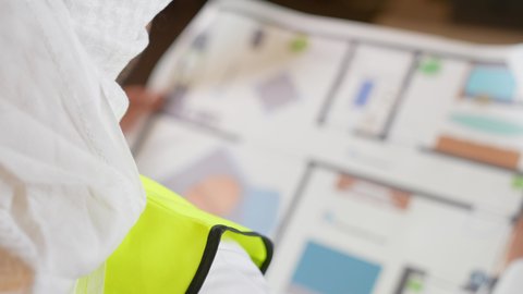 إتقان إدارة المشاريع باستخدام الحاسوب المحمول، العمل في القطاع الهندسي، مفهوم الهندسة والانشاءات المعماريه، تصوير مقرب من الجانب لمهندس عربي خليجي قطري يرتدي الثوب التقليدي والغتره مع سترة الحماية يجلس خلف طاولة المكتب وأمامه المخطط وبجانبه الخوذة