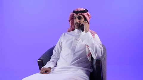 التواصل مع الأفراد عبر الانترنت,استخدام التقنيات والأجهزة الحديثة والتكنولوجيا، إجراء المكالمات الهاتفية عبر الجوال، دردشة ومحادثات مع الأصدقاء، تصوير لرجل عربي خليجي بحريني يرتدي الثوب التقليدي والشماغ يجلس على كرسي مريح