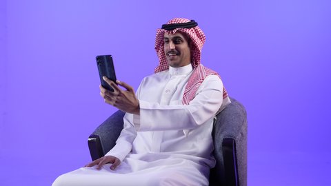 إجراء المكالمات الهاتفية عبر الجوال، استخدام التقنيات والأجهزة الحديثة والتكنولوجيا، التواصل مع الأفراد عبر الانترنت, دردشة ومحادثات مع الأصدقاء، تصوير لرجل عربي خليجي بحريني يرتدي الثوب التقليدي والشماغ يجلس على كرسي مريح
