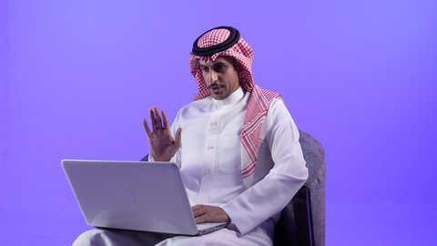 إجراء مكالمات الفيديو باستخدام الحاسوب المحمول، إقامة اجتماعات العمل عن بعد عبر الانترنت،مفهوم التوظيف أونلاين, دمج التقنية بالأعمال الإدارية، تصوير لرجل عربي خليجي بحريني يرتدي الثوب التقليدي والشماغ يجلس على كرسي