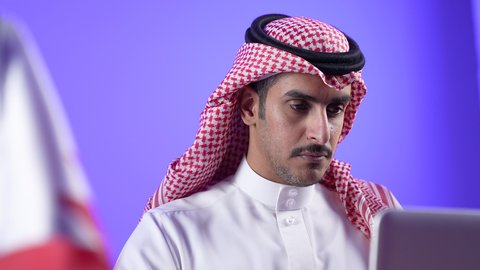 إقامة اجتماعات العمل عن بعد عبر الانترنت، إجراء مكالمات الفيديو باستخدام الحاسوب المحمول، مفهوم التوظيف أونلاين, دمج التقنية بالأعمال الإدارية، تصوير لرجل عربي خليجي بحريني يرتدي الثوب التقليدي والشماغ يجلس على كرسي