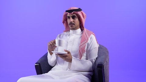 محاولة الحصول على القليل من الراحة، التلذذ بكوب من الشاي الساخن، الاسترخاء وتناول مشروبات دافئة، تصوير لشاب عربي خليجي بحريني يرتدي الثوب التقليدي والشماغ يجلس على كرسي ويمسك بيده فنجان من مشروبه المفضل