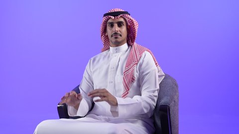 مفهوم الاناقة والاهتمام بالمظهر الخارجي, ايماءات الشعور بالحيرة وعدم التأكد، تصوير لرجل عربي خليجي بحريني يرتدي الثوب التقليدي والشماغ يجلس على كرسي مريح بتعابير ايدي متلامسة، شاب سعودي ينظر الى الكاميرا بتعابير السرور