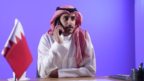 اجراء مكالمه هاتفيه ، دمج التقنية بالأعمال الإدارية، إجراء مكالمات الفيديو باستخدام الهاتف المحمول، إقامة اجتماعات العمل عن بعد عبر الانترنت، مفهوم التوظيف أونلاين,  تصوير لرجل عربي خليجي بحريني يرتدي الثوب التقليدي والشماغ يجلس على كرسي
