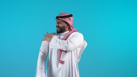 Nerve and muscle aches and pains, request for help and need for treatment, a young Saudi man feeling pain in his muscles and joints, a picture of an Arab Gulf Bahraini man wearing a traditional thobe and shemagh, putting his hand on his shoulder with a gesture of fatigue and exhaustion, an emergency medical case