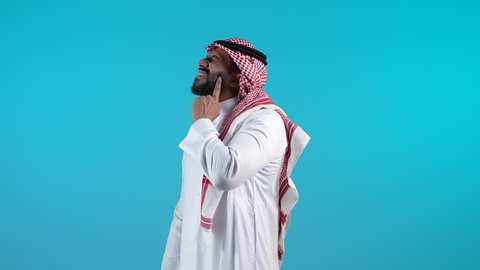 A Saudi man looks up with gestures of thinking and confusion, contemplation and concentration to find a solution to a problem, feeling bored and distressed, problems and decision making, a picture of a young Bahraini Gulf Arab man wearing the traditional thobe and shemagh, putting his hand behind his chin