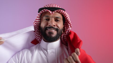 تصوير لرجل عربي خليجي قطري يحمل علم قطر بايماءات الفخروالاعتزاز، حب الوطن والانتماء إليه، رموز وثقافات وطنية, الاحتفال باليوم الوطني القطري 18 ديسمبر، إحياء ذكرى تأسيس الدولة، خلفية ملونه