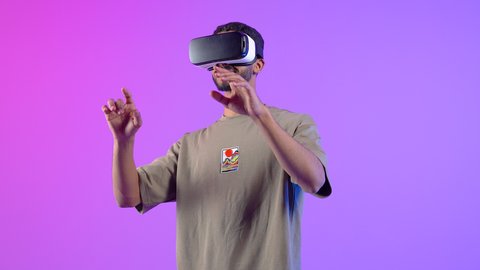 Interaction and simulation of the imaginary world, an Omani man watching movies through virtual reality glasses pointing his finger at something, portrait of a young Saudi Arabian Gulf man wearing casual clothes and 3D virtual reality glasses, colorful background