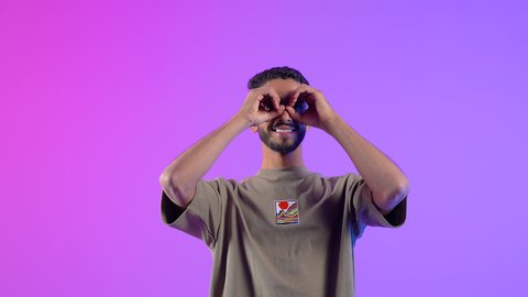 Love of adventure and exploration, future planning for goals and ambitions, portrait of a young Arab Gulf Omani man wearing casual clothes, putting his hand over his eye in the form of a telescope, a Saudi man seeing distant objects, colorful background
