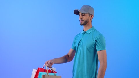 Online shopping and ordering, online delivery networks in the Gulf, integrating business with technology, portrait of a young Arab Gulf Omani man wearing casual clothes and a gray hat working as a sales representative, a Saudi man delivering orders, blue background