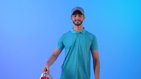 الشحن والتوصيل ذات الجودة العالية، بورتريه لشاب عربي خليجي سعودي يرتدي الزي الكاجوال ويضع قبعة رماضية يعمل كمندوب مبيعات، رجل عربى خليجي عماني يحمل بيده شنط كرتونية، عملية توصيل الطلبات للزبائن, خلفية زرقاء