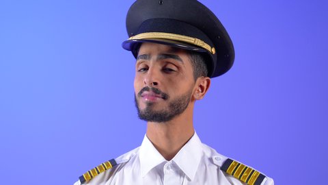 طاقم الاستقبال والترحيب بالركاب، العمل في مجال الطيران، رحلات جوية سياحية, خطوط الطيران العمانية, بورتريه مقرب لكابتن طيار عربي خليجي عماني مبتسم يرتدي الزي الرسمي يقف باستقامة ينظر الى الكاميرا بتعابير السعادة والسرور، خلفية زرقاء