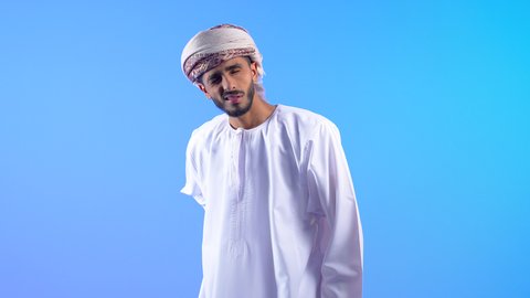 تعابير الوجه تدل على الاضطراب والتألم من الكتفين، آلام المفاصل والعظام والعمود الفقري، بورتريه لرجل عربي خليجي عماني يرتدي الدشداشة و العمامة يمسك كتفه بإيماءات الألم, الحاجة للراحة والحصول على العلاج، خلفية زرقاء