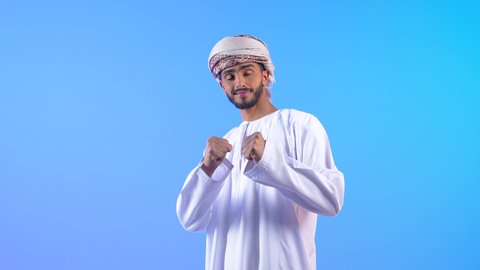 إتقان فنون الملاكمة، ممارسة رياضة الدفاع عن النفس، زيادة قدرة العضلات على التحمل، بورتريه لشاب عربي خليجي عماني يرتدي الدشداشة و العمامة ينظر الى الكاميرا يرفع قبضات يديه بإيماءات القوة، ، خلفية زرقاء