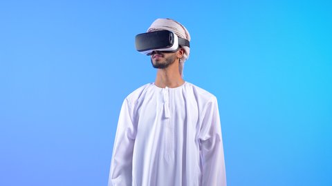 التطور التقني والتكنولوجي, المتعة و التسلية بالمشاهدة عبر نظارة الواقع الافتراضي، بورتريه لشاب عربي خليجي عماني يرتدي الدشداشه و العمامة ينظر من خلال نظارات ثلاثية الأبعاد (الفي ار), الاندماج ومحاكاة العالم الخيالي والنظر الى الافلام الواقعيه، خلفية زرقاء