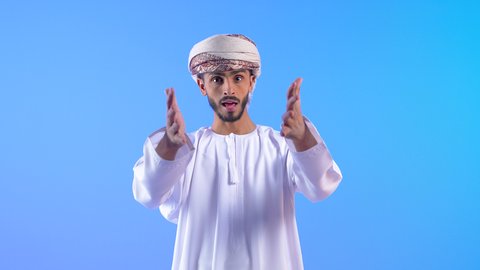 النقاش الحاد والمواجهة، الضغط العصبي و التوتر, تعابير التوبيخ والغضب, بورتريه لشاب عربي خليجي عماني يرتدي الدشداشة يرفع يده بإيماءات إلقاء اللوم، طلب التوقف عن فعل الأخطاء، الشعور بالإنزعاج والرغبة بالإنتقام، خلفية زرقاء