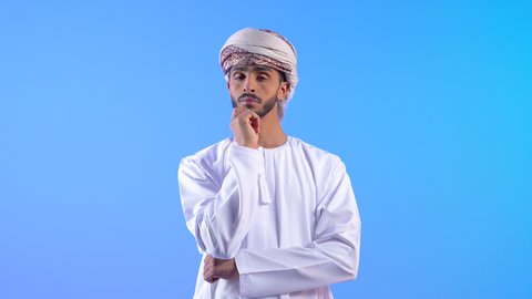 Confusion and inability to make decisions, facial expressions indicating difficulty in determining the situation, portrait of an Omani man wearing a dishdasha and turban showing signs of confusion, thinking and expressing an opinion, blue background