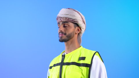مفهوم الإشراف على المشاريع الإنشائية، إدارة الأعمال والاطلاع على آخر المستجدات، بورتريه من الجانب لمهندس عربي خليجي عماني  مبتسم يرتدي الدشداشة والسترة و العمامة يمسك المخطط و الخوذة بيده، التأكد من سير العمل بالشكل المطلوب والصحيح، خلفية زرقاء