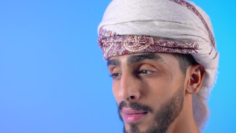 الاهتمام بالمظهر الخارجي، مفهوم إدراة الأعمال والمشاريع، بورتريه مقرب لشاب عربي خليجي عماني يرتدي الدشداشة و العمامه مبتسم يقوم بقرءاة اوراق العمل ، خلفيه زرقاء