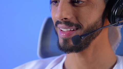 التواصل مع الأهل والأصدقاء، استخدام التكنولوجيا والأجهزة التقنية الحديثة المتطورة، مفهوم الإصغاء والإستماع, بورتريه مقرب لشاب عربي خليجي عماني مبتسم يرتدي الدشداشة و العمامة يقوم بالتحدث عبر الميكروفون, خلفية زرقاء