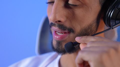 Using modern advanced technology and technical devices, chatting with family and friends, the concept of listening and hearing, a close-up portrait of a smiling young Arab Gulf Omani man wearing a dishdasha and turban speaking into a microphone, blue background