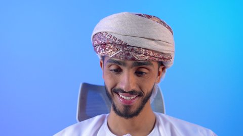 إمكانية تسديد الفواتير عبر بطاقة الصراف، الشراء والدفع عن طريق بطاقات الإئتمان البنكية, بورتريه مقرب لشاب عربي خليجي عماني يرتدي الزي الدشداشة و العمامة يجلس على الطاولة و بجانبة التابلت يمسك بيده البطاقة الالكترونية, خلفية زرقاء