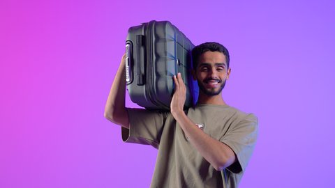 الذهاب في جولات سياحية ترفيهية في إجازة الصيف, بورتريه مقرب لشاب عربي سعودي خليجي يرتدي الزي الكاجوال يحمل حقيبة السفر على كتفه, الاستعداد لقضاء رحلة صيفية ممتعة, النظر إلى الكاميرا بإيماءات الفرحه و السرور، خلفية ملونة