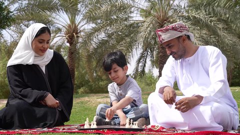مفهوم التركيز والتحدي ،اوقات التسليه والمتعه ، تصوير لعائلة عربية خليجية عمانية تلعب لعبة الشطرنج ،  نزهه في الهواء الطلق ، الجلوس في الطبيعة الخضراء ، أنشطة ترفيهية عائلية