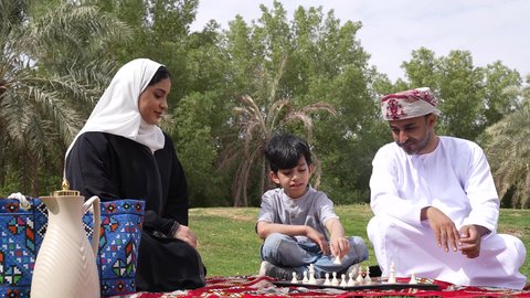 تصوير لعائلة عربية خليجية عمانية تلعب لعبة الشطرنج ، مفهوم التركيز والتحدي ،اوقات التسليه والمتعه ، نزهه في الهواء الطلق ، الجلوس في الطبيعة الخضراء ، أنشطة ترفيهية عائلية
