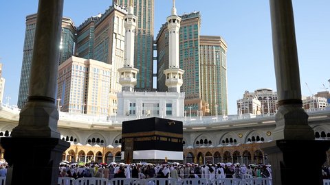 The Qiblah of Islam and Muslims, performing the Hajj and Umrah rituals, the destination of Muslims from all over the world, a sacred Islamic religious place and landmark in Saudi Arabia, the concept of worship and drawing closer to God, pilgrims and Umrah performers circumambulating the Kaaba in Mecca, the Kingdom Tower and the hotel towers overlooking the Haram