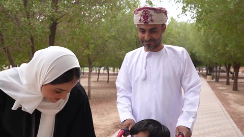 تصوير لعائلة عربية خليجية عمانية تقوم بمساعدة طفل يجلس على الكرسي المتحرك، تأمين ادوات ومعدات تساعد أصحاب الهمم على التنقل والحركة، الاستمتاع بالأجواء الصيفيه المشمسة، التنزه في احدى الحدائق العامة