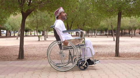 التنزه في احدى الحدائق العامة، توفير اجهزة ومعدات تساعد بالحركة والتنقل ، العنايه بأصحاب الهمم وتأمين احتياجاتهم الخاصة، تصوير لشاب عربي خليجي عماني مقعد يرتدي الكمه و الدشداشة يجلس على كرسي متحرك