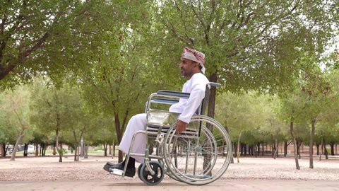 توفير اجهزة ومعدات تساعد بالحركة والتنقل ، العنايه بأصحاب الهمم وتأمين احتياجاتهم الخاصة، تصوير لشاب عربي خليجي عماني مقعد يرتدي الكمه و الدشداشة يجلس على كرسي متحرك