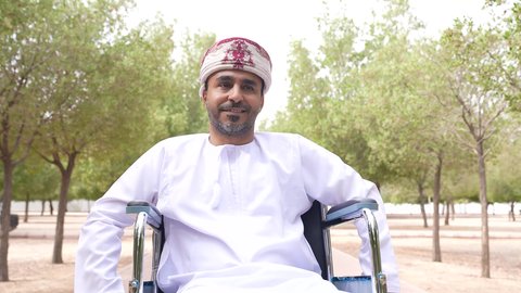 Caring for people with disabilities and providing for their special needs, a picture of a disabled young Gulf Arab Omani man wearing a cloak and a dishdasha sitting in a wheelchair, providing devices and equipment that help with movement and mobility